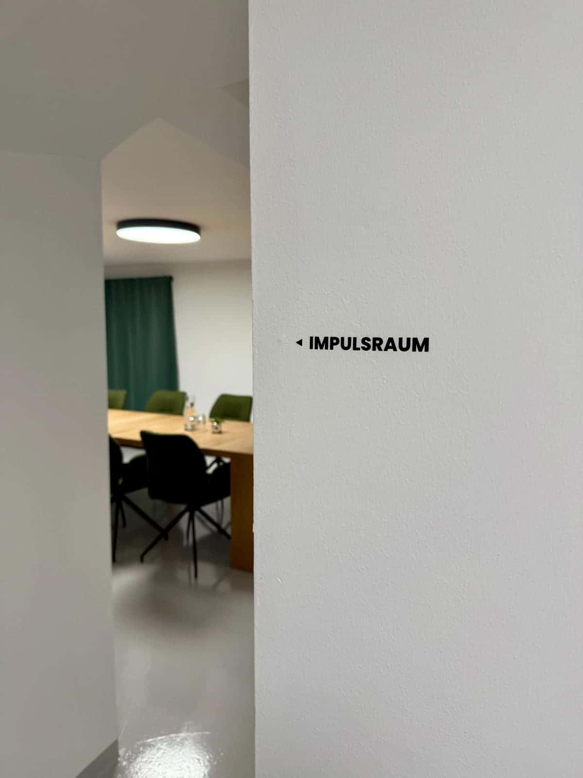 Der Impulsraum: Besprechungsraum mit großem Holztisch und grünen Stühlen
